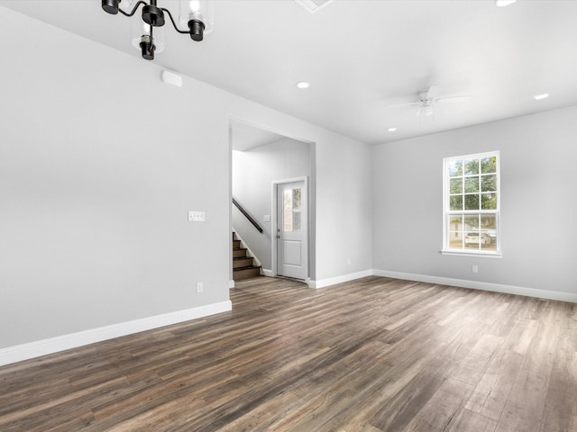 empty room with dark hardwood / wood-style flooring and ceiling fan with notable chandelier