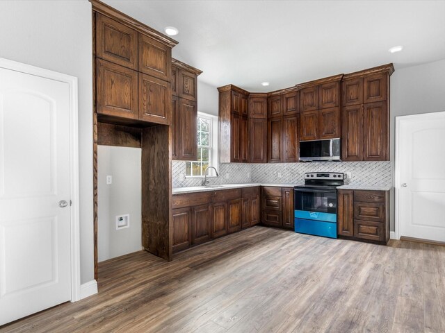 kitchen with sink, backsplash, dark brown cabinets, appliances with stainless steel finishes, and light wood-type flooring