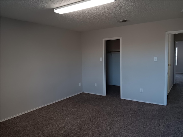 unfurnished bedroom featuring a closet, a walk in closet, dark carpet, and a textured ceiling