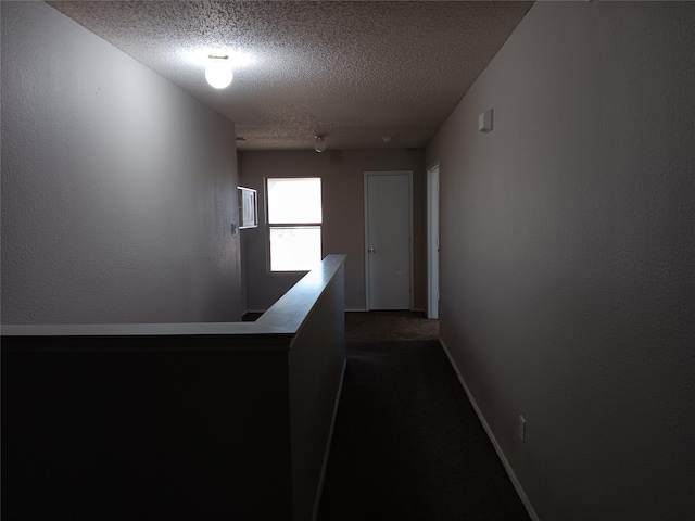 hallway with dark colored carpet and a textured ceiling