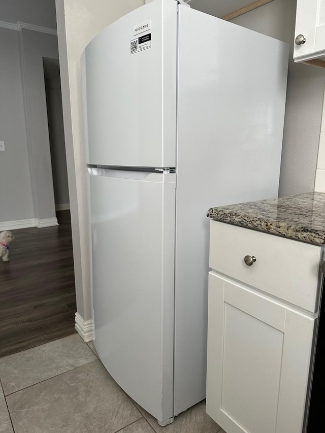 kitchen featuring baseboards, dark stone counters, ornamental molding, freestanding refrigerator, and white cabinetry