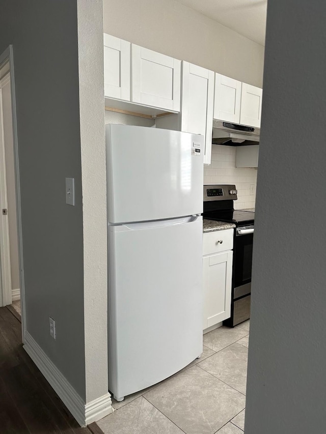 kitchen featuring under cabinet range hood, white cabinetry, stainless steel range with electric cooktop, freestanding refrigerator, and decorative backsplash