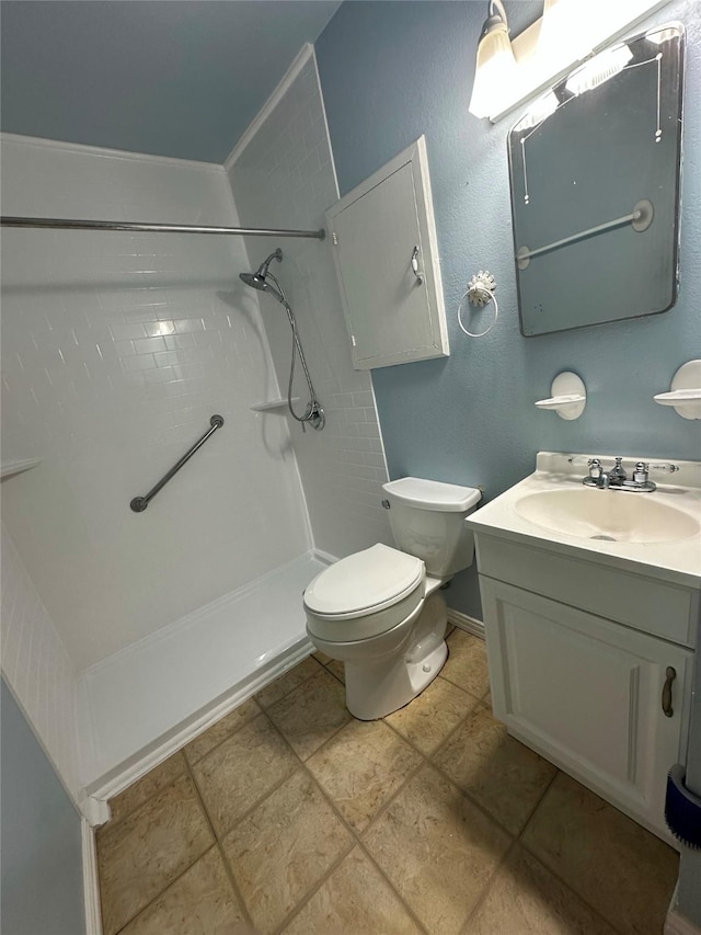 bathroom featuring vanity, a tile shower, tile patterned floors, and toilet