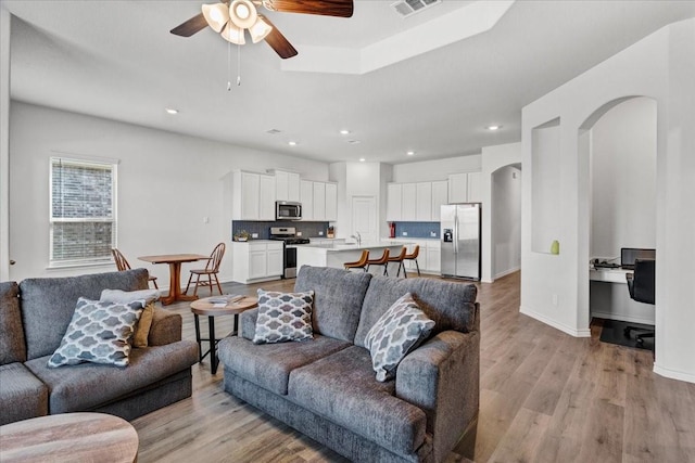 living room with ceiling fan, sink, and light wood-type flooring