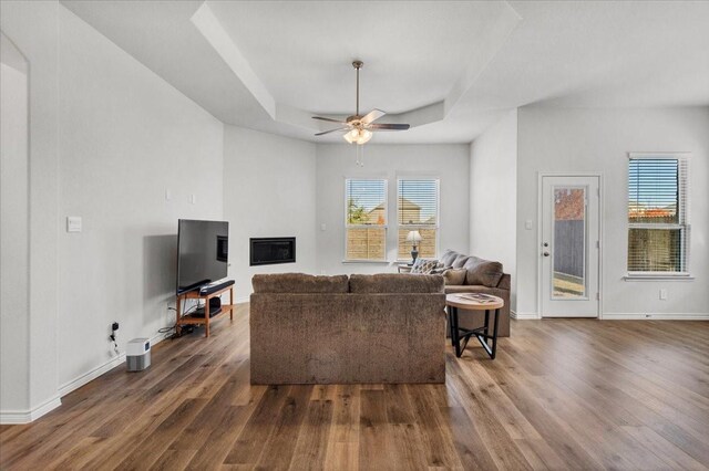 living room featuring a tray ceiling, ceiling fan, and dark wood-type flooring