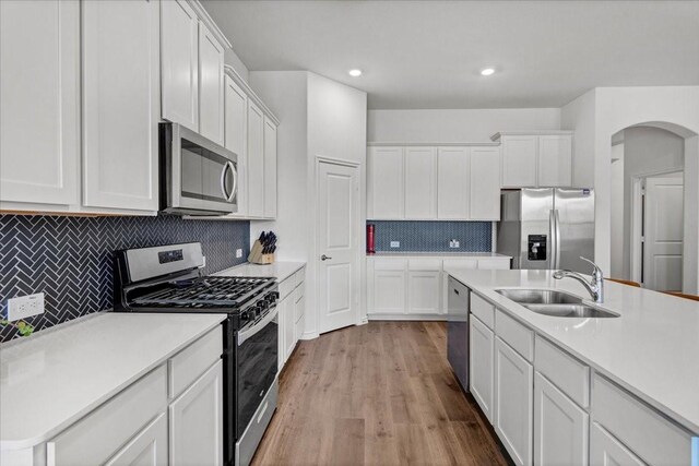 kitchen featuring white cabinetry, sink, tasteful backsplash, light hardwood / wood-style flooring, and appliances with stainless steel finishes