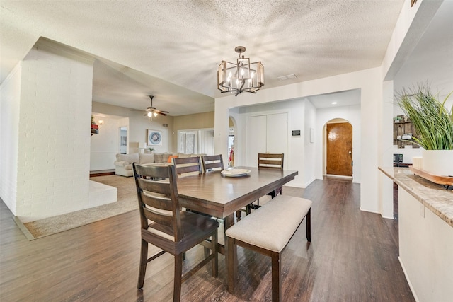 dining area with a textured ceiling, ceiling fan with notable chandelier, and dark hardwood / wood-style floors