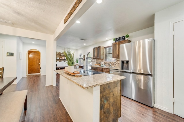 kitchen featuring decorative backsplash, a textured ceiling, stainless steel appliances, hardwood / wood-style floors, and a kitchen island