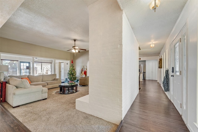 living room featuring crown molding, wood-type flooring, a textured ceiling, ceiling fan, and brick wall