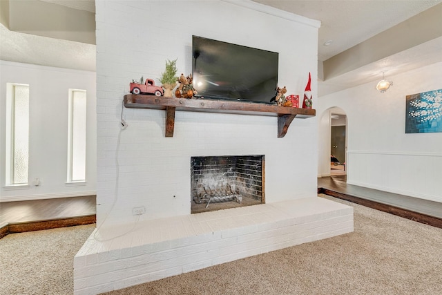 living room with carpet flooring, wooden walls, a textured ceiling, and a brick fireplace