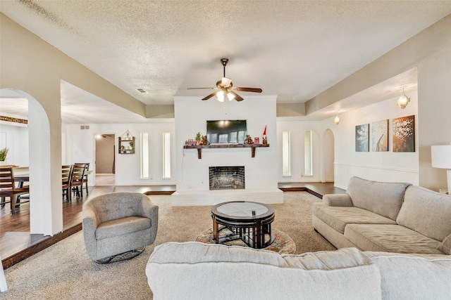 living room with hardwood / wood-style flooring, ceiling fan, a fireplace, and a textured ceiling