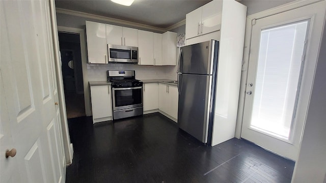 kitchen with dark wood-type flooring, white cabinets, ornamental molding, tasteful backsplash, and stainless steel appliances