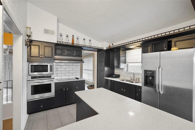 kitchen with lofted ceiling, sink, decorative backsplash, a textured ceiling, and appliances with stainless steel finishes