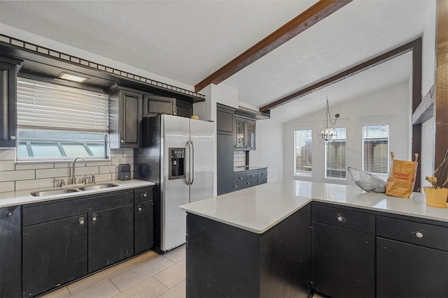 kitchen featuring stainless steel refrigerator with ice dispenser, backsplash, sink, lofted ceiling with beams, and an inviting chandelier