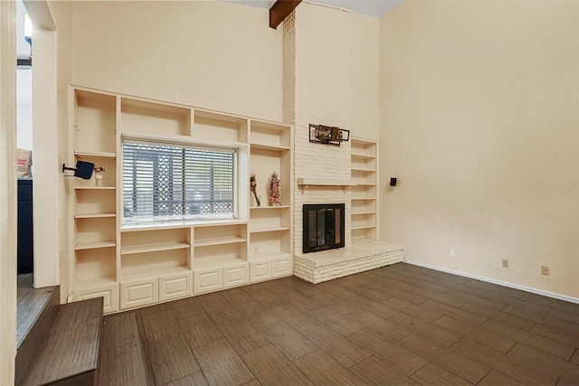 unfurnished living room with dark hardwood / wood-style floors, beam ceiling, a high ceiling, and a brick fireplace