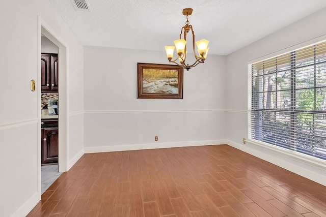 spare room featuring hardwood / wood-style flooring, a textured ceiling, and a notable chandelier