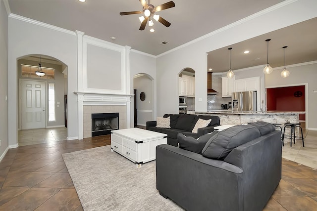 tiled living room featuring ceiling fan, crown molding, and a tiled fireplace