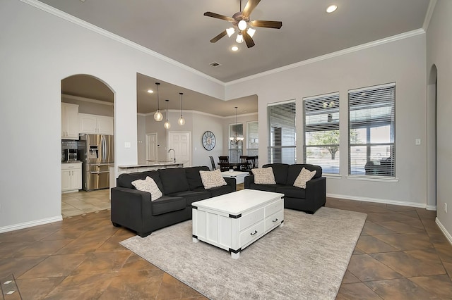 living room featuring arched walkways, dark tile patterned flooring, a ceiling fan, baseboards, and crown molding