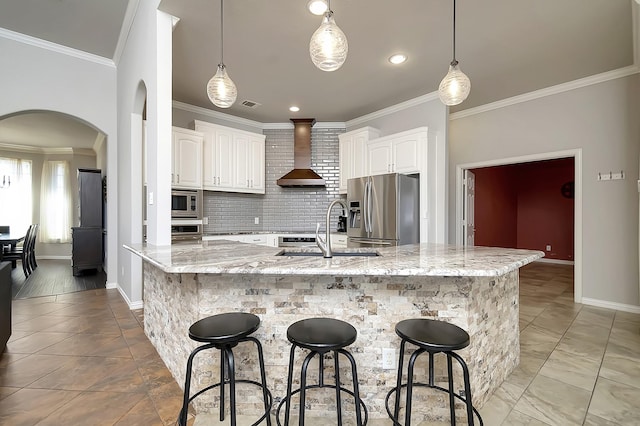 kitchen featuring a sink, ornamental molding, wall chimney range hood, appliances with stainless steel finishes, and decorative backsplash