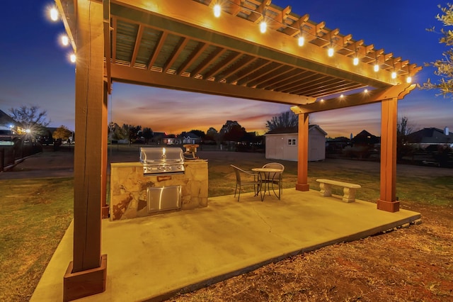 patio terrace at dusk with area for grilling, a storage unit, and exterior kitchen