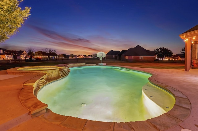 pool at dusk featuring an in ground hot tub and a patio