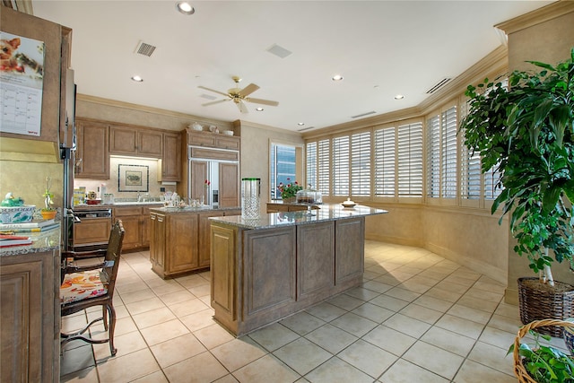 kitchen with a kitchen island, ornamental molding, light tile patterned floors, light stone counters, and paneled refrigerator