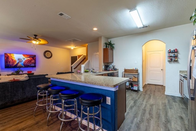 kitchen with kitchen peninsula, a kitchen breakfast bar, ceiling fan, sink, and hardwood / wood-style floors