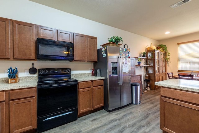 kitchen featuring black appliances, light stone counters, and light hardwood / wood-style flooring