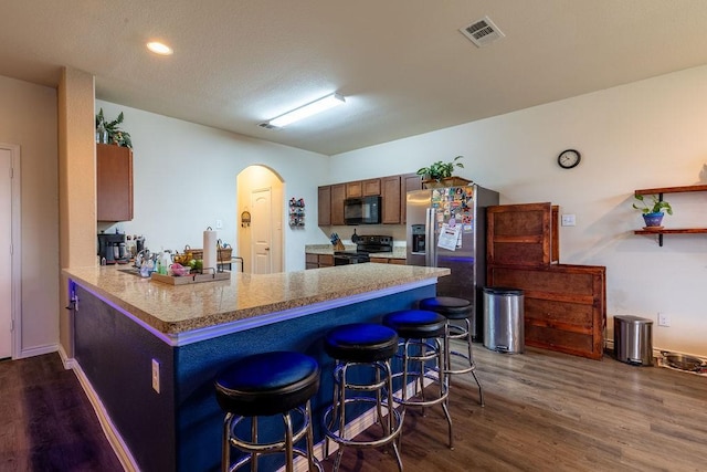 kitchen with light stone countertops, dark hardwood / wood-style flooring, kitchen peninsula, a breakfast bar, and black appliances