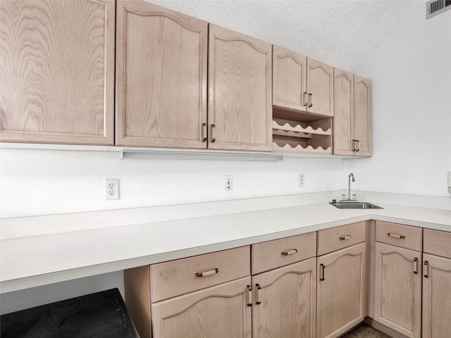 kitchen with sink, a textured ceiling, light brown cabinetry, and vaulted ceiling