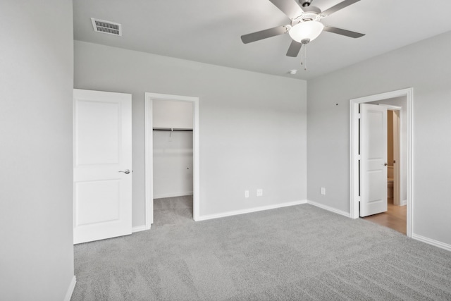 unfurnished bedroom featuring a walk in closet, ceiling fan, a closet, and carpet floors