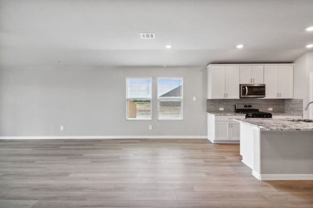 kitchen featuring light stone countertops, tasteful backsplash, light hardwood / wood-style floors, white cabinets, and appliances with stainless steel finishes