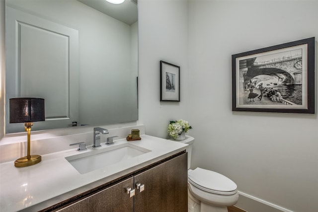 half bathroom with baseboards, vanity, and toilet