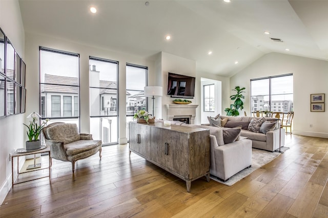 living area featuring high vaulted ceiling, light wood-type flooring, a fireplace, and recessed lighting