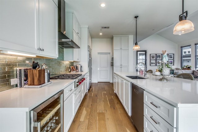 kitchen featuring light wood-style flooring, appliances with stainless steel finishes, a sink, wall chimney range hood, and beverage cooler