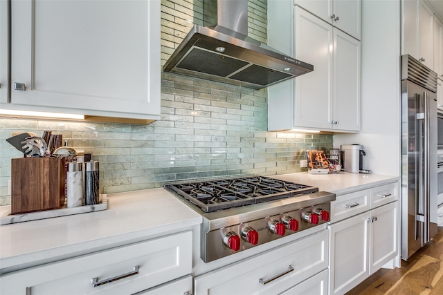 kitchen featuring tasteful backsplash, light countertops, appliances with stainless steel finishes, white cabinetry, and wall chimney exhaust hood