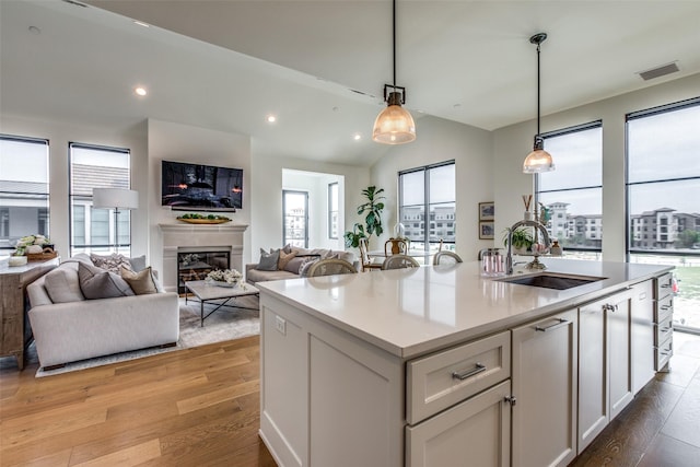 kitchen featuring visible vents, a glass covered fireplace, light countertops, light wood-style floors, and a sink