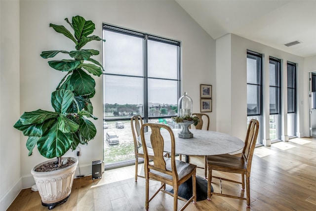 dining room featuring lofted ceiling, hardwood / wood-style flooring, visible vents, and baseboards