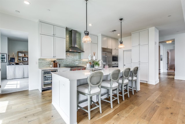 kitchen featuring built in appliances, wine cooler, visible vents, light wood-style floors, and wall chimney range hood