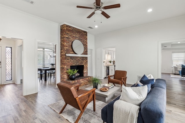 living room featuring sink, a brick fireplace, light hardwood / wood-style flooring, ceiling fan, and ornamental molding