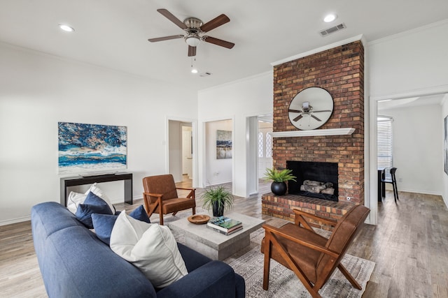 living room featuring hardwood / wood-style floors, ceiling fan, crown molding, and a brick fireplace