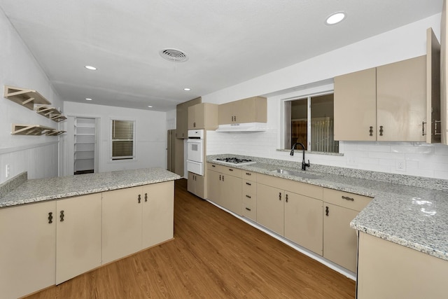 kitchen featuring sink, decorative backsplash, light stone counters, light hardwood / wood-style floors, and white appliances