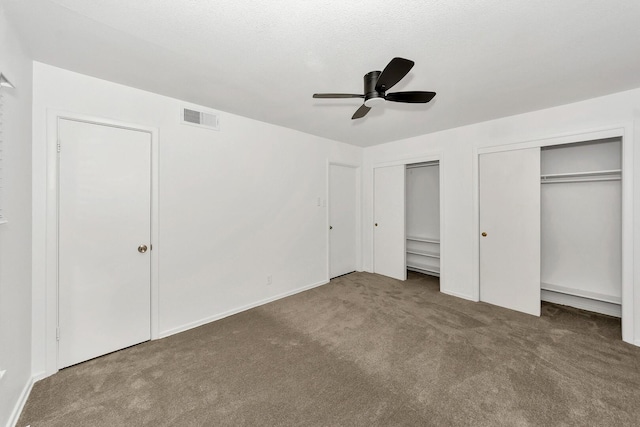 unfurnished bedroom featuring dark colored carpet, a textured ceiling, two closets, and ceiling fan