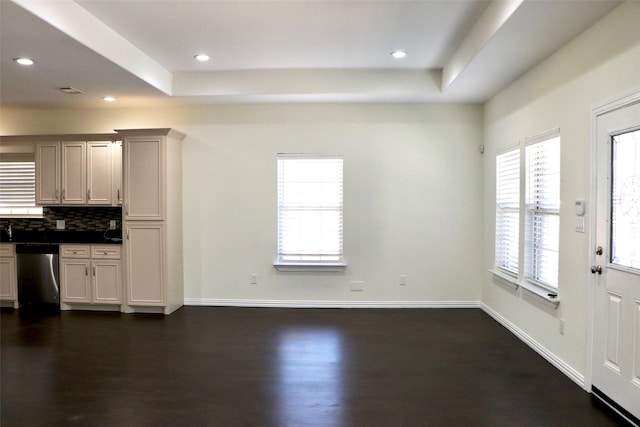 interior space with backsplash, a raised ceiling, dark hardwood / wood-style flooring, and stainless steel dishwasher