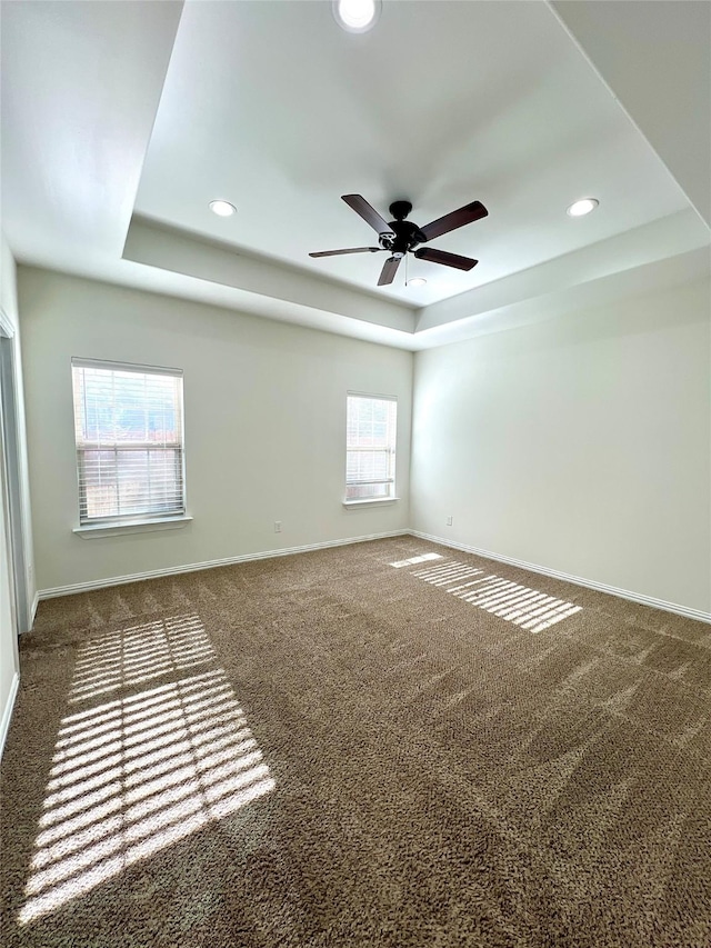 spare room with dark colored carpet, a tray ceiling, and ceiling fan