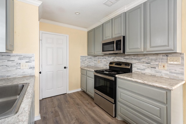 kitchen with ornamental molding, appliances with stainless steel finishes, gray cabinets, decorative backsplash, and dark wood finished floors