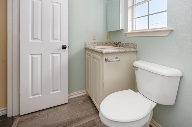 half bath featuring toilet, baseboards, wood finished floors, and vanity