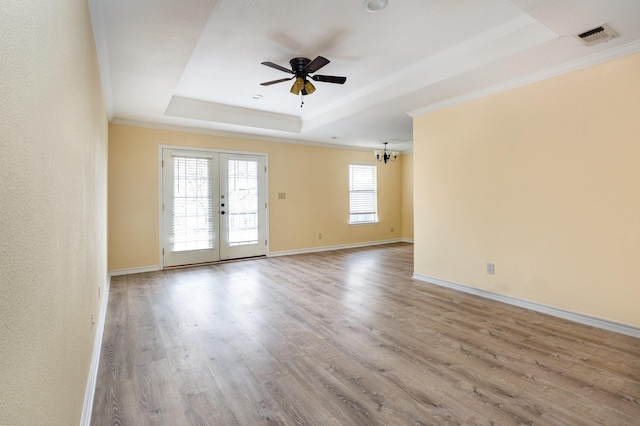 empty room with visible vents, a raised ceiling, ornamental molding, french doors, and light wood-style floors