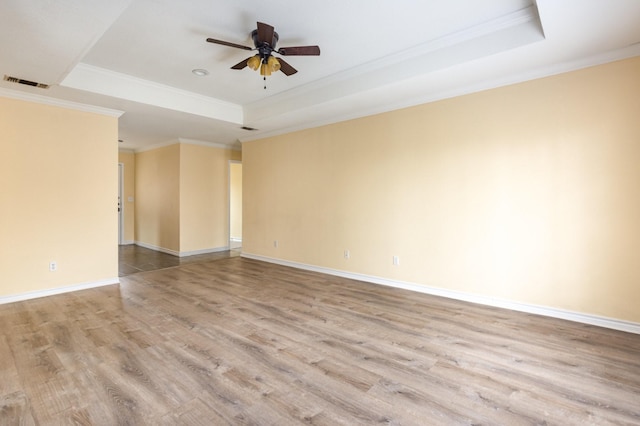 empty room featuring ceiling fan, visible vents, baseboards, light wood-style floors, and a tray ceiling