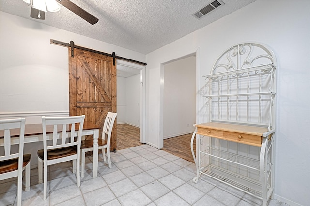 dining area featuring light tile patterned flooring, ceiling fan, a barn door, and a textured ceiling